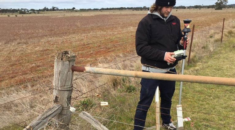 Land surveyor using a GNSS receiver to check a boundary corner beside an old post-and-wire fence